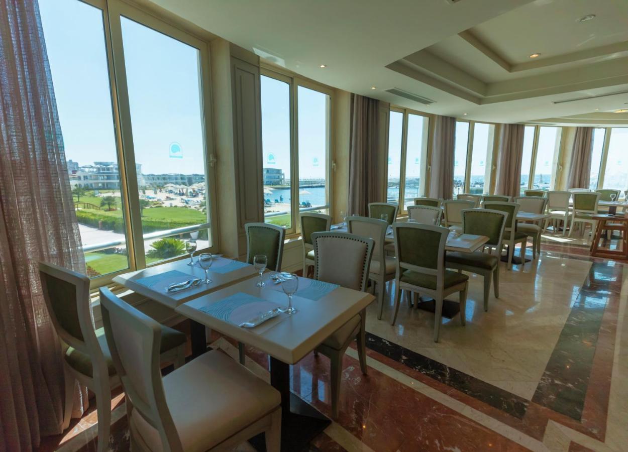 Sunrise Alex Avenue Hotel Alexandria Exterior foto The photo shows an elegant restaurant interior with several tables and chairs arranged in a spacious setting. The dining area features large windows that allow natural light to flood in, offering a view of the outdoor landscape. The tables are set wi