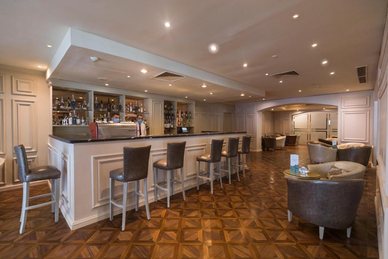 Sunrise Alex Avenue Hotel Alexandria Exterior foto The photo shows a modern bar area with a sleek, minimalist design. The bar itself features a long countertop with several high-backed chairs positioned in front of it. Behind the bar, shelves are lined with various bottles of alcoholic beverages. The