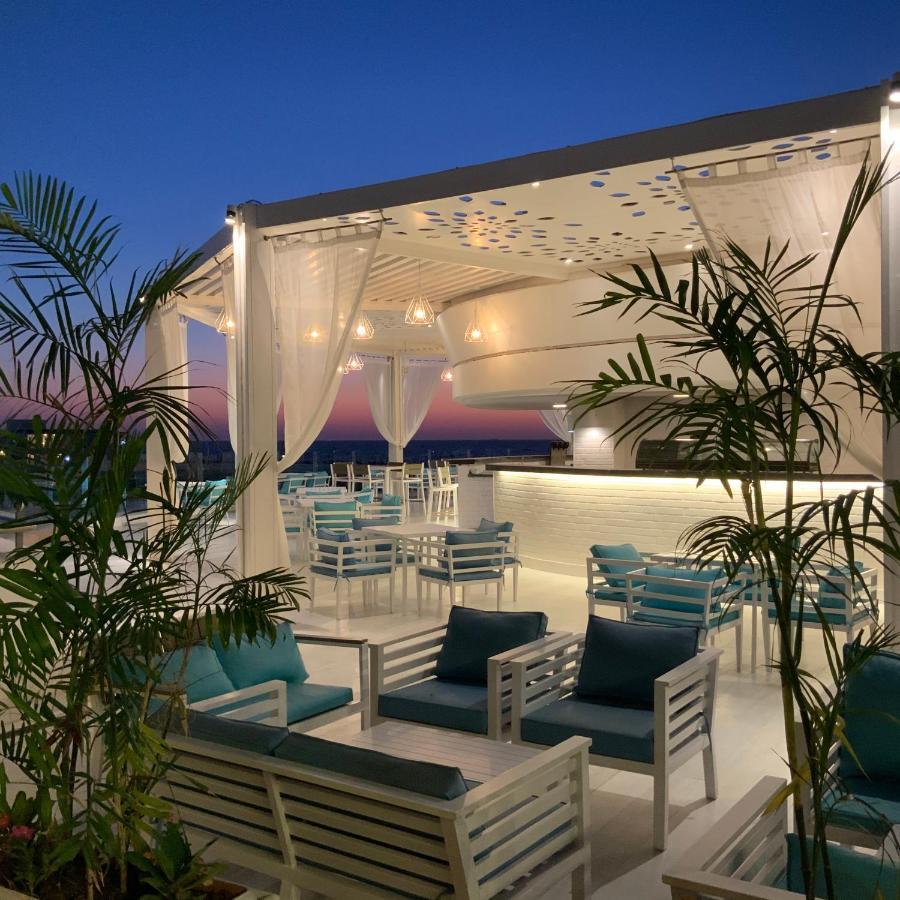 Sunrise Alex Avenue Hotel Alexandria Exterior foto The photo shows a stylish outdoor terrace or rooftop lounge area. It features white furniture, including comfortable seating with teal cushions. The space is adorned with draped sheer curtains, providing a relaxed and elegant atmosphere. Lush green p