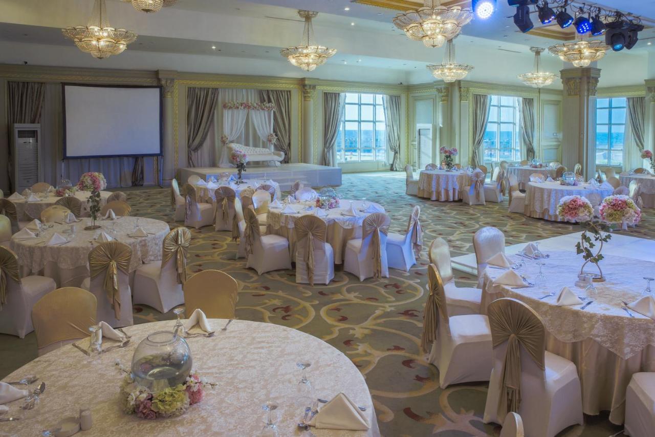 Sunrise Alex Avenue Hotel Alexandria Exterior foto The photo shows an elegantly designed banquet hall set up for an event. There are several round tables covered with light-colored tablecloths, each adorned with decorative centerpieces, such as floral arrangements. The chairs are draped with fabric t