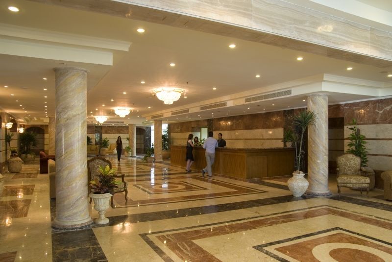 Sunrise Alex Avenue Hotel Alexandria Exterior foto The photo shows the interior of a spacious lobby, likely in a hotel. There are marble floors with intricate patterns, elegant lighting fixtures, and tall pillars. In the center, there is a reception desk where staff members are attending to guests. S
