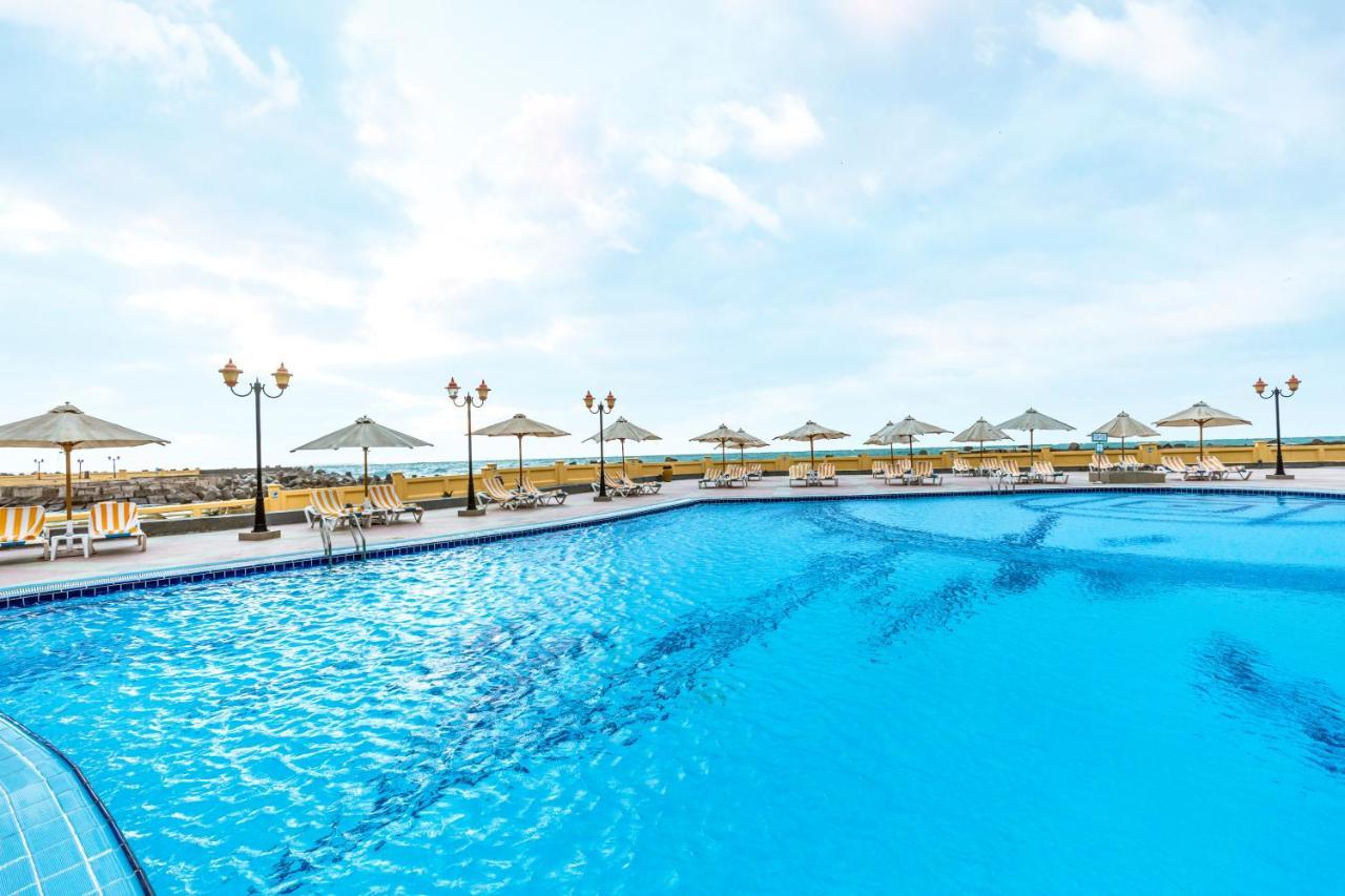 Sunrise Alex Avenue Hotel Alexandria Exterior foto The photo shows a large swimming pool with crystal clear blue water. Surrounding the pool are several sun loungers and umbrellas, providing shade for relaxation. In the background, there appear to be more lounge chairs and additional umbrellas, sugge
